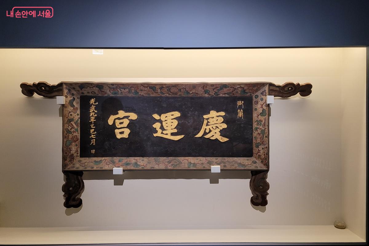 &lsquo;慶運宮&rsquo;이라 쓰인 경운궁 현판이 전시 공간 벽면에 걸려 있는 모습.