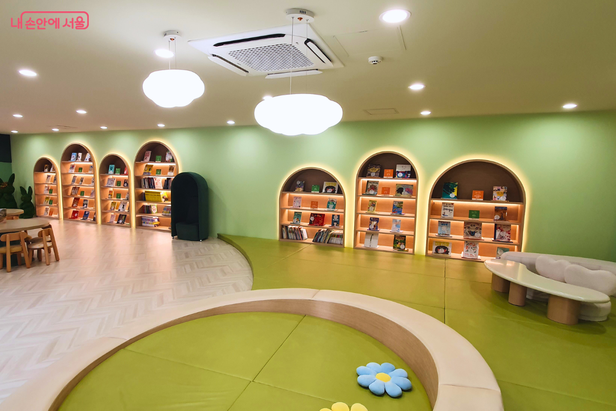 연두색 벽면에 아치형 서가가 배치된 용산서가 어린이 도서관 내부다. 천장에는 구름 모양 조명이 달려 있고 바닥에는 아이들이 놀 수 있는 연두색 매트 공간이 마련되어 있다.
