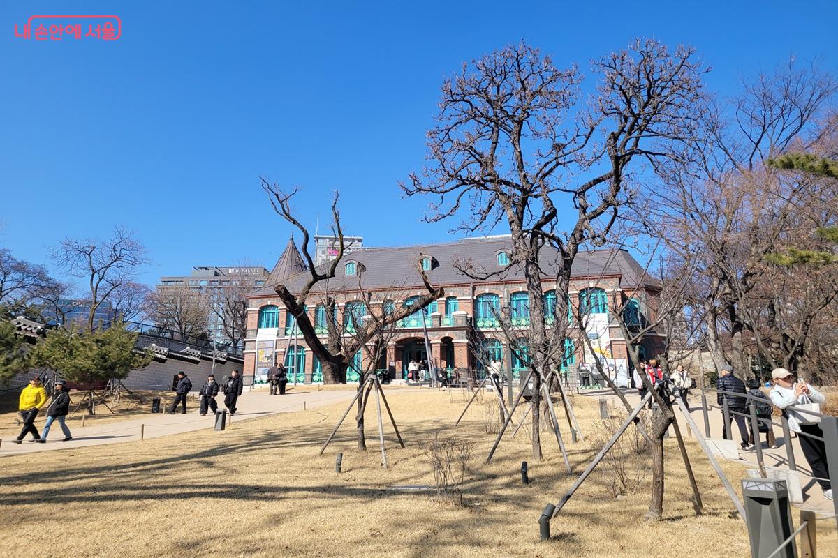 덕수궁 돈덕전 붉은 벽돌 건물 앞 잔디 마당에서 시민들이 산책하며 전시를 관람하는 모습.