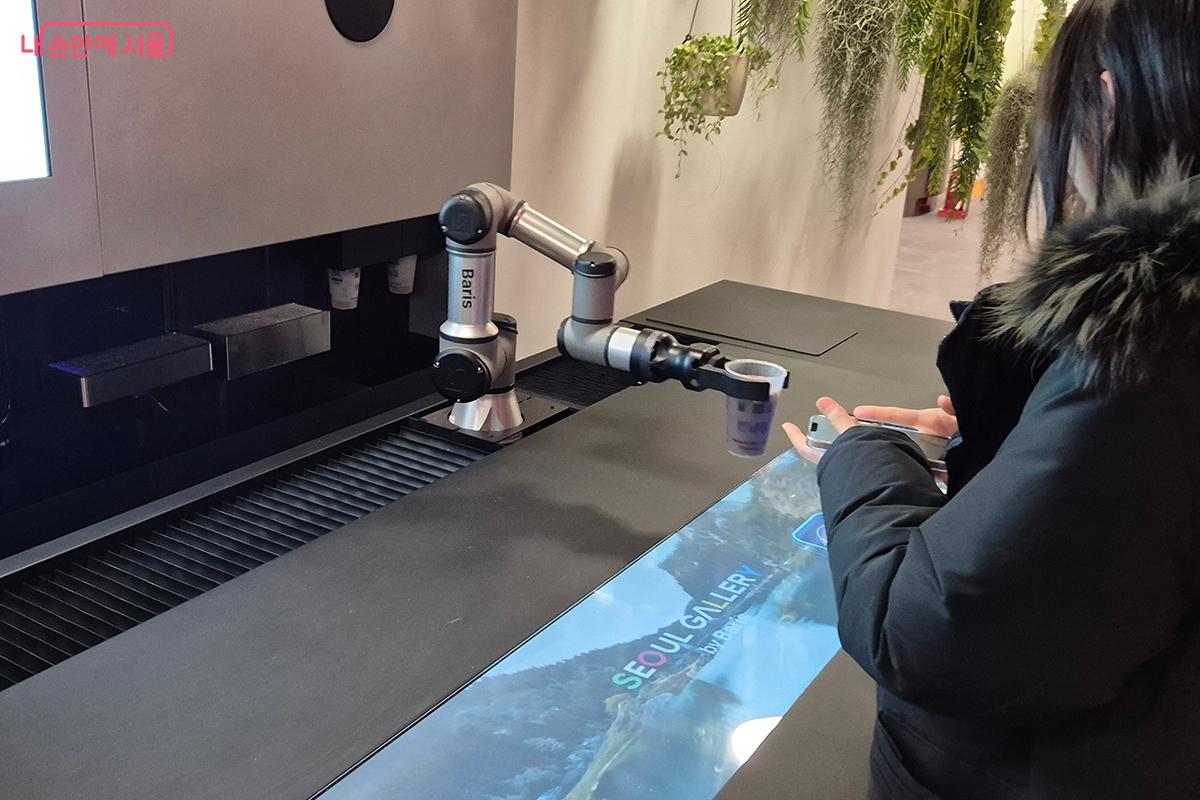 완성된 커피를 구매자에게 전달하고 있는 로봇팔의 모습