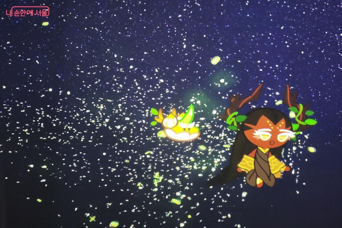 어두운 배경에 쿠키런 캐릭터와 빛나는 그래픽 효과가 표현된 전시 영상 화면 모습.