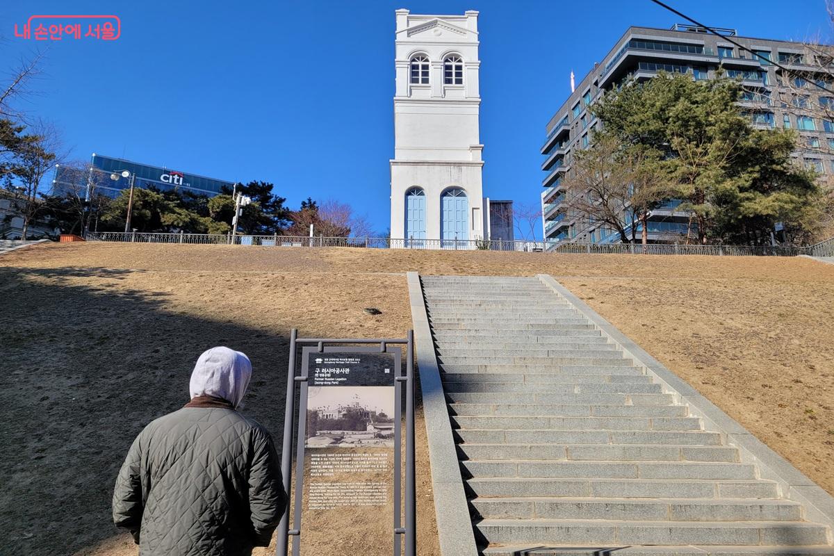 정동에 위치한 구 러시아공사관 터의 흰색 탑형 건물과 계단, 안내판을 바라보는 방문객의 모습.