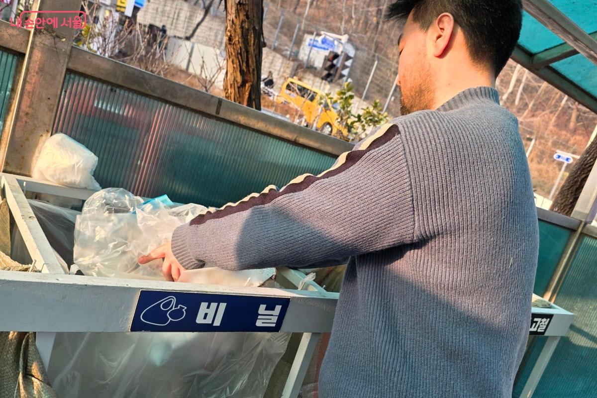 야외 분리수거장에서 투명 페트병을 전용 수거함에 넣는 모습입니다. 비닐 라벨을 깨끗이 제거한 상태로 배출하고 있습니다.