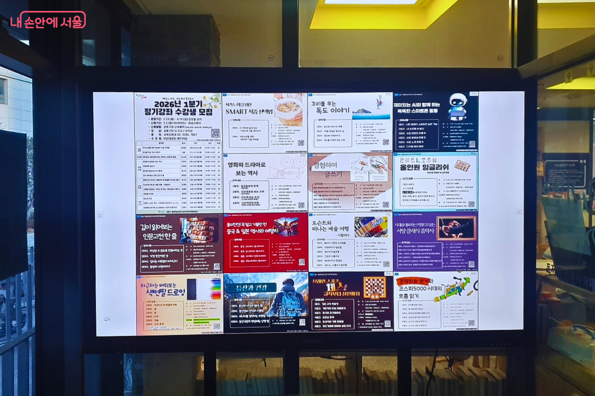 센터 내부 로비에 설치된 대형 디지털 안내 화면이다. '2026년 1분기 정기강좌 수강생 모집' 안내를 비롯하여 스마트폰 활용, 독도 이야기, 글쓰기, 인문 고전, 예술 여행 등 16개의 다양한 교육 프로그램 홍보 포스터가 4x4 배열로 질서 정연하게 표출되고 있다. &copy;양정화