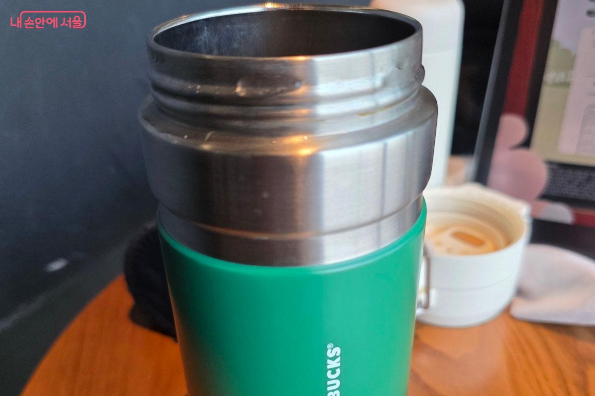카페에서 일회용 컵 대신 초록색 개인 텀블러를 사용하여 음료를 주문한 모습입니다.