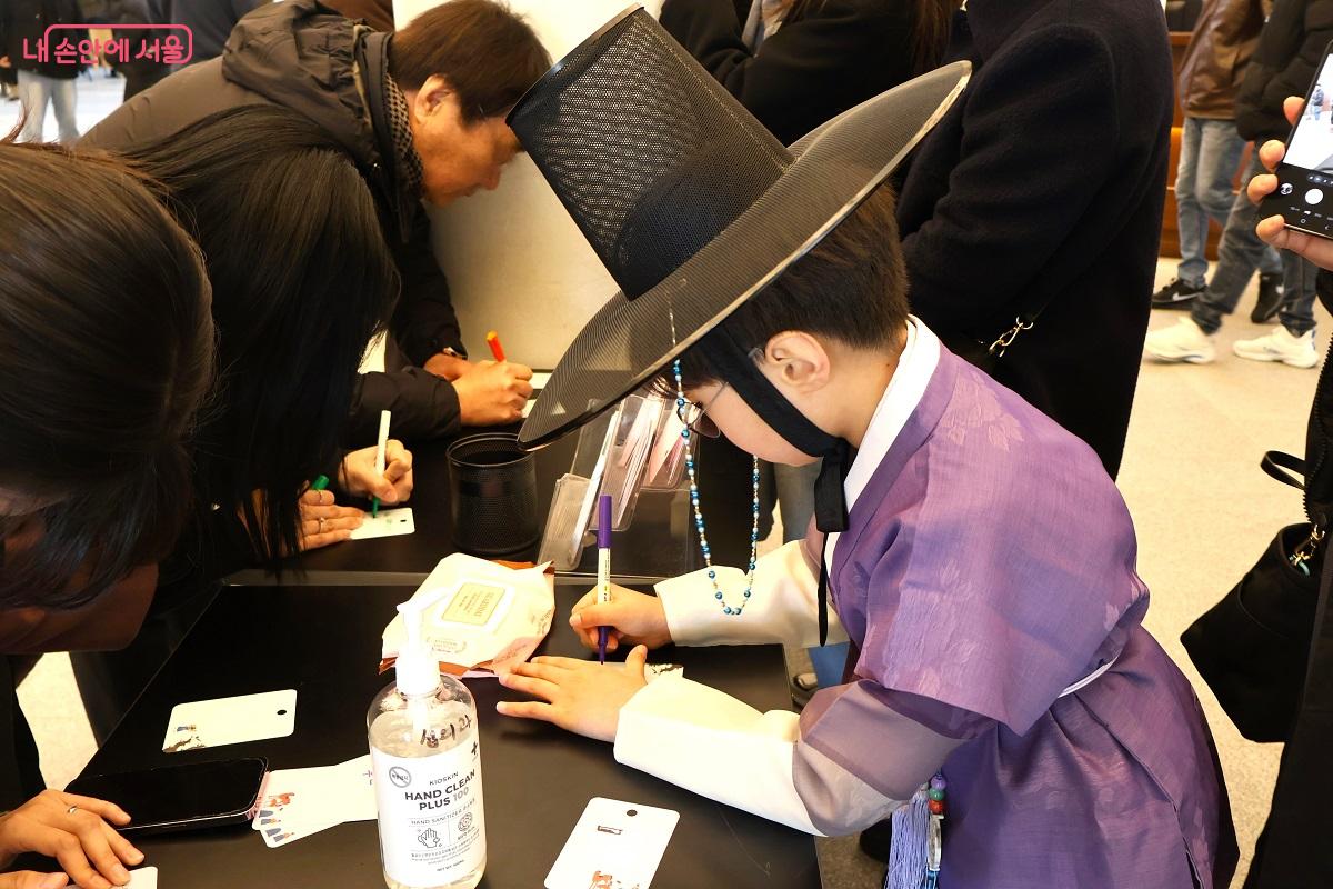 박물관 1층 로비에 마련된 체험 코너에서 한복을 정갈하게 차려입은 어린이가 진지한 표정으로 새해의 소망을 적고 있다. &copy;김대진