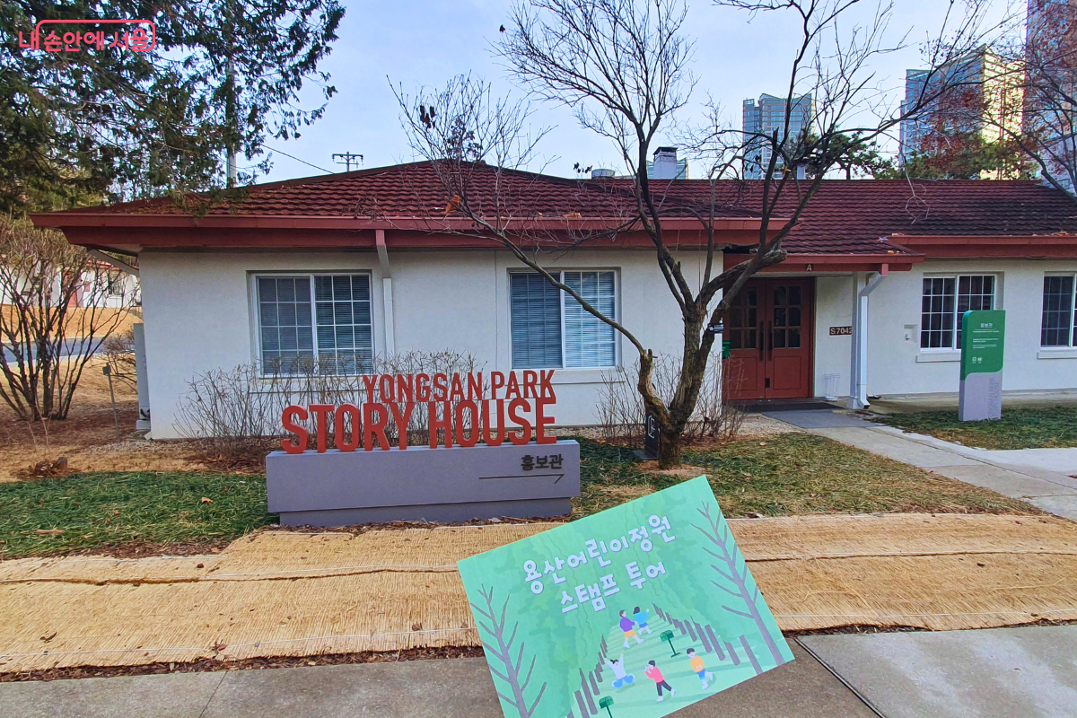 'YONGSAN PARK STORY HOUSE'라고 적힌 붉은색 조형물이 있는 용산공원 스토리하우스 앞이다. 앞마당에는 어린이용 스탬프 투어 안내판이 세워져 있다.