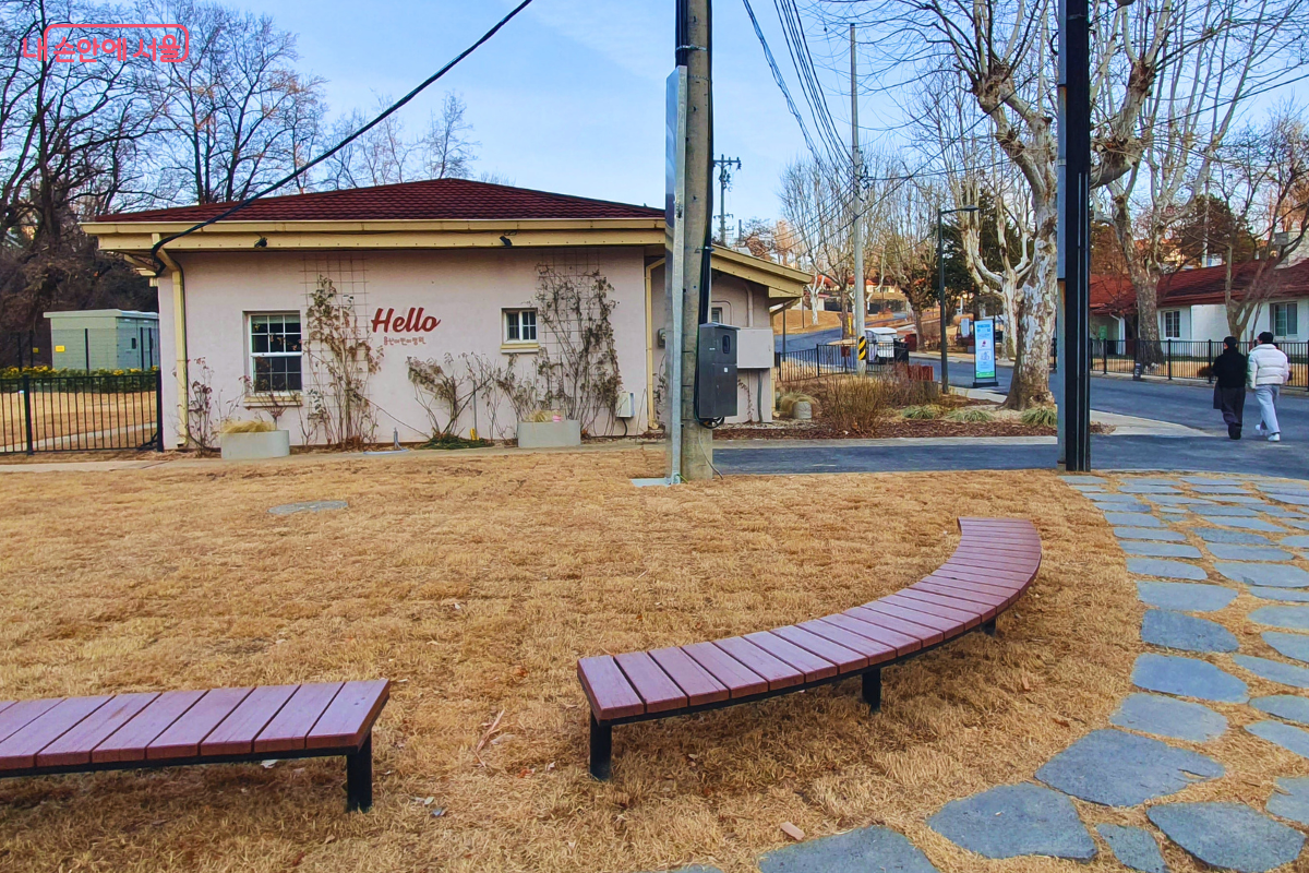 붉은 지붕과 분홍색 외벽이 조화를 이루는 단층 건물인 종합안내센터 외관이다. 벽면에는 'Hello'라는 환영 문구가 적혀 있고 앞마당에는 곡선형 나무 벤치가 놓여 있다.