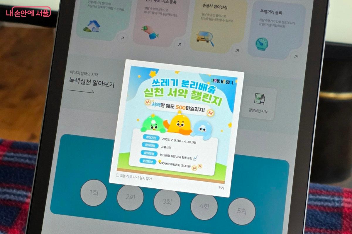 태블릿 PC 화면에 시민 서약 참여를 독려하는 팝업창이 떠 있습니다. 귀여운 캐릭터와 함께 캠페인 안내 문구가 적혀 있습니다.