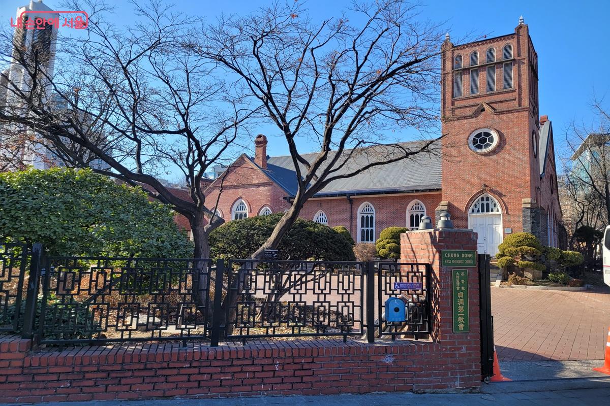 정동제일교회 붉은 벽돌 건물과 종탑, 나무와 담장이 함께 보이는 모습.