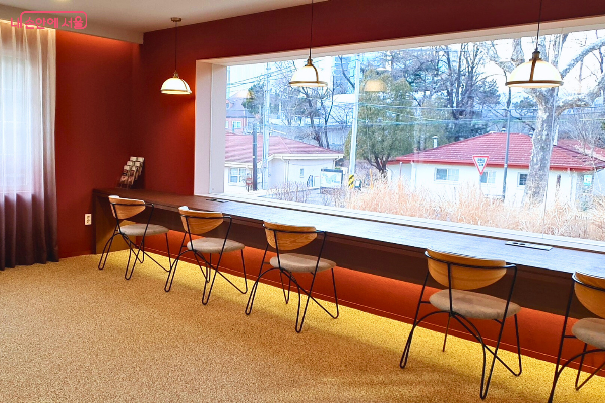 붉은색 벽면과 따뜻한 조명이 어우러진 용산서가 성인용 도서관 내부다. 긴 원목 테이블이 창가를 따라 배치되어 정원 밖 풍경을 보며 독서하기 좋다.