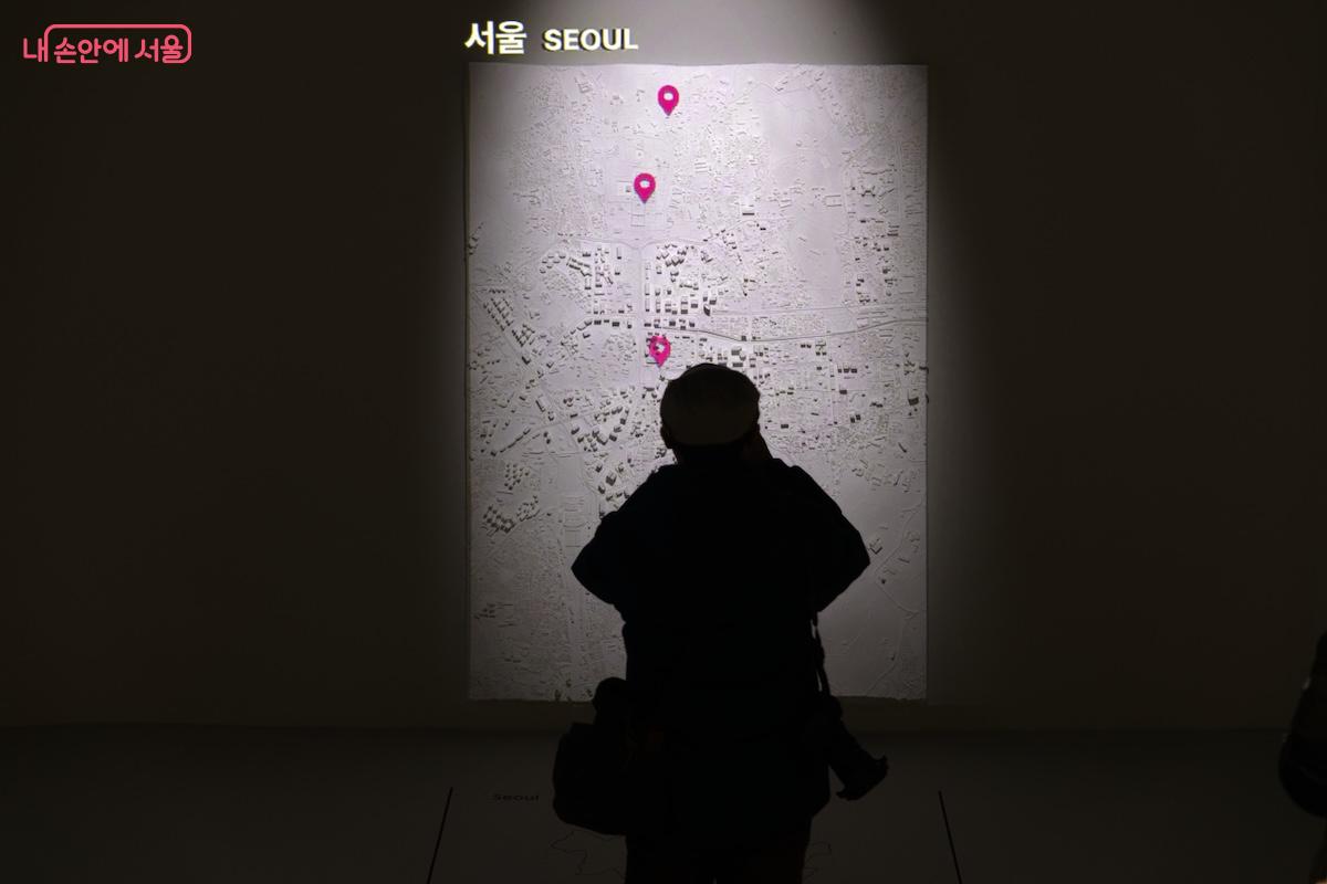 입체적인 도면처럼 느껴지는 서울의 모습을 사진으로 찍고 있는 관람객