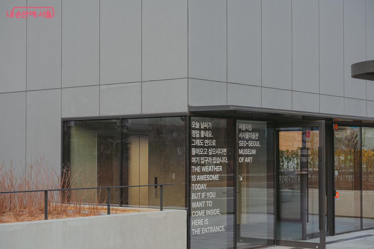 미술관 옥상정원 유리창. '오늘 날씨가 정말 좋네요. 그래도 안으로 들어오고 싶으시다면 여기 입구가 있습니다'라는 흰색 텍스트가 썬팅되어 있다.