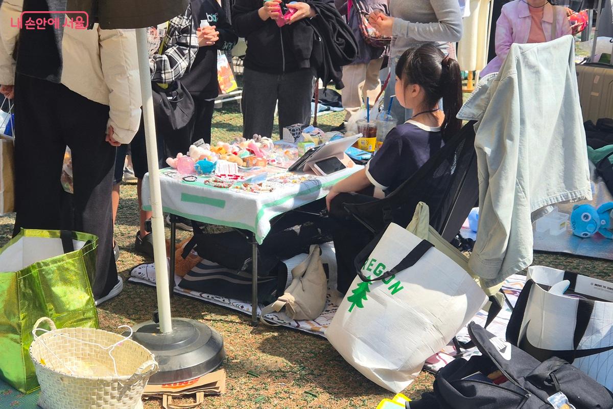 판매 물품이 놓인 테이블을 어린이 한 명이 지키고 있다. 구경하는 시민들을 바라보며 말을 건네지 못하고 망설이는 모습이 귀엽게 느껴진다. ©마가은