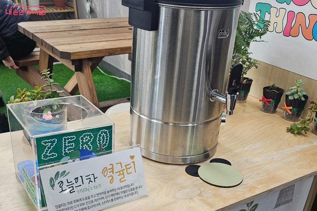 탁자 위에 따뜻한 차를 담아둘 수 있는 보온통이 놓여 있고, 옆에는 &lsquo;오늘의 차:영귤티 &rsquo; 안내문이 함께 배치되어 있다. 누구나 편안하게 차를 마시며 쉬어갈 수 있는 공간의 분위기를 느낄 수 있다. &copy;최동열