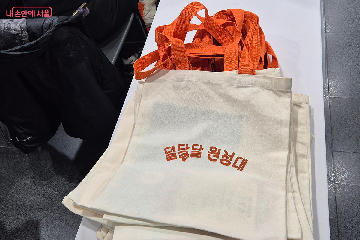 참가자들이 기념품으로 받은 '덜 달달 원정대' 문구가 인쇄된 주황색 끈의 커스텀 에코백 &copy;백승훈