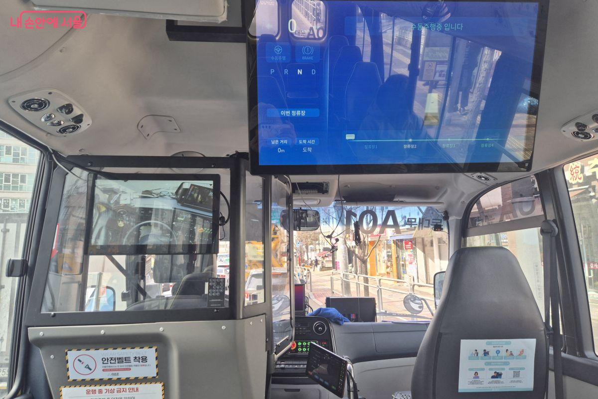 버스 앞쪽에 현재 운행 정보를 알 수 있는 모니터와 운전석을 볼 수 있는 화면