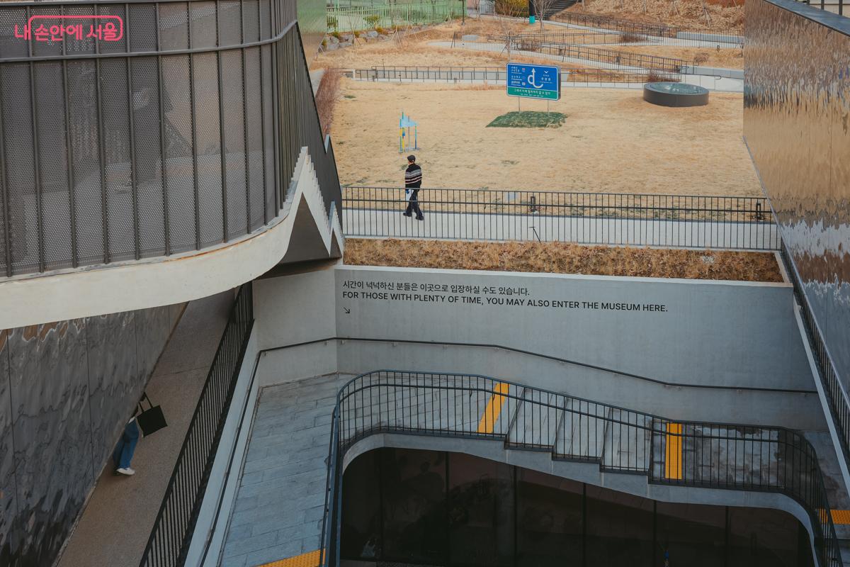 미술관 외부 계단 벽면. '시간이 넉넉하신 분들은 이곳으로 입장하실 수도 있습니다'라는 글귀와 아래를 향한 화살표가 적혀 있다.
