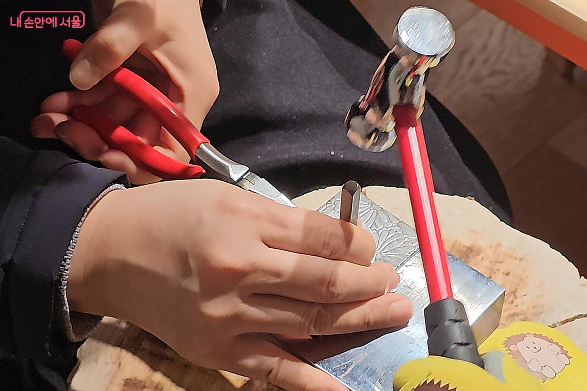 망치로 두들겨 펜던트에 장식과 이름을 새기는 아빠와 어린이 &copy;오도연