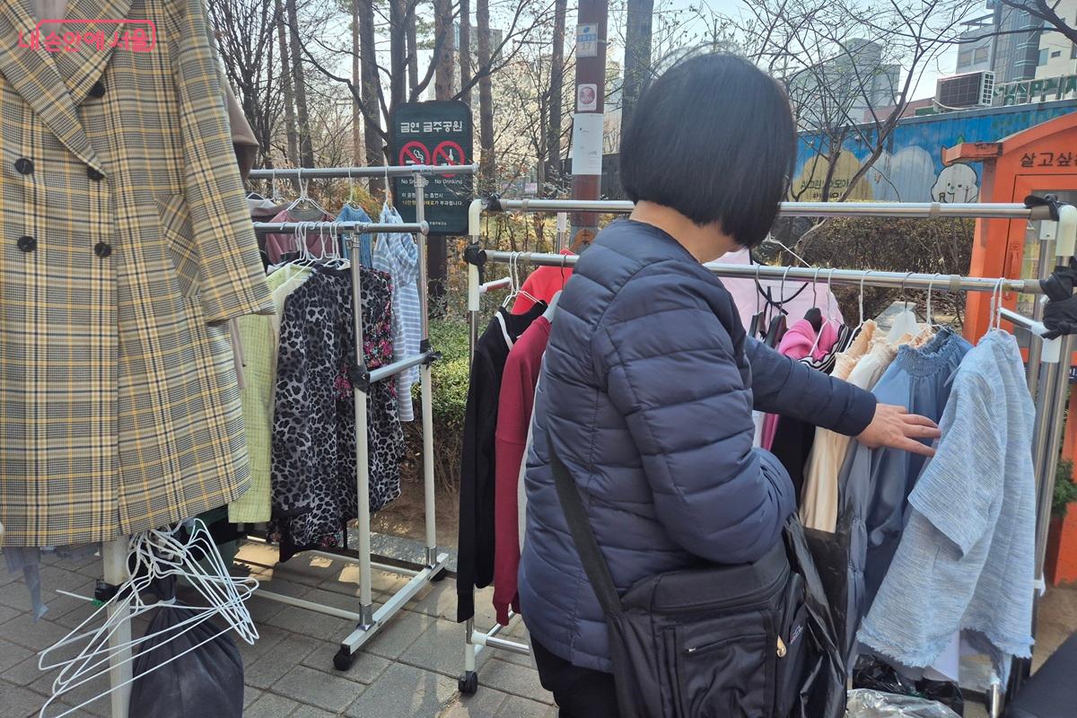 공원 산책로에 설치된 행거에 다양한 옷이 걸려 있고, 한 시민이 이를 살펴보고 있다. ©마가은