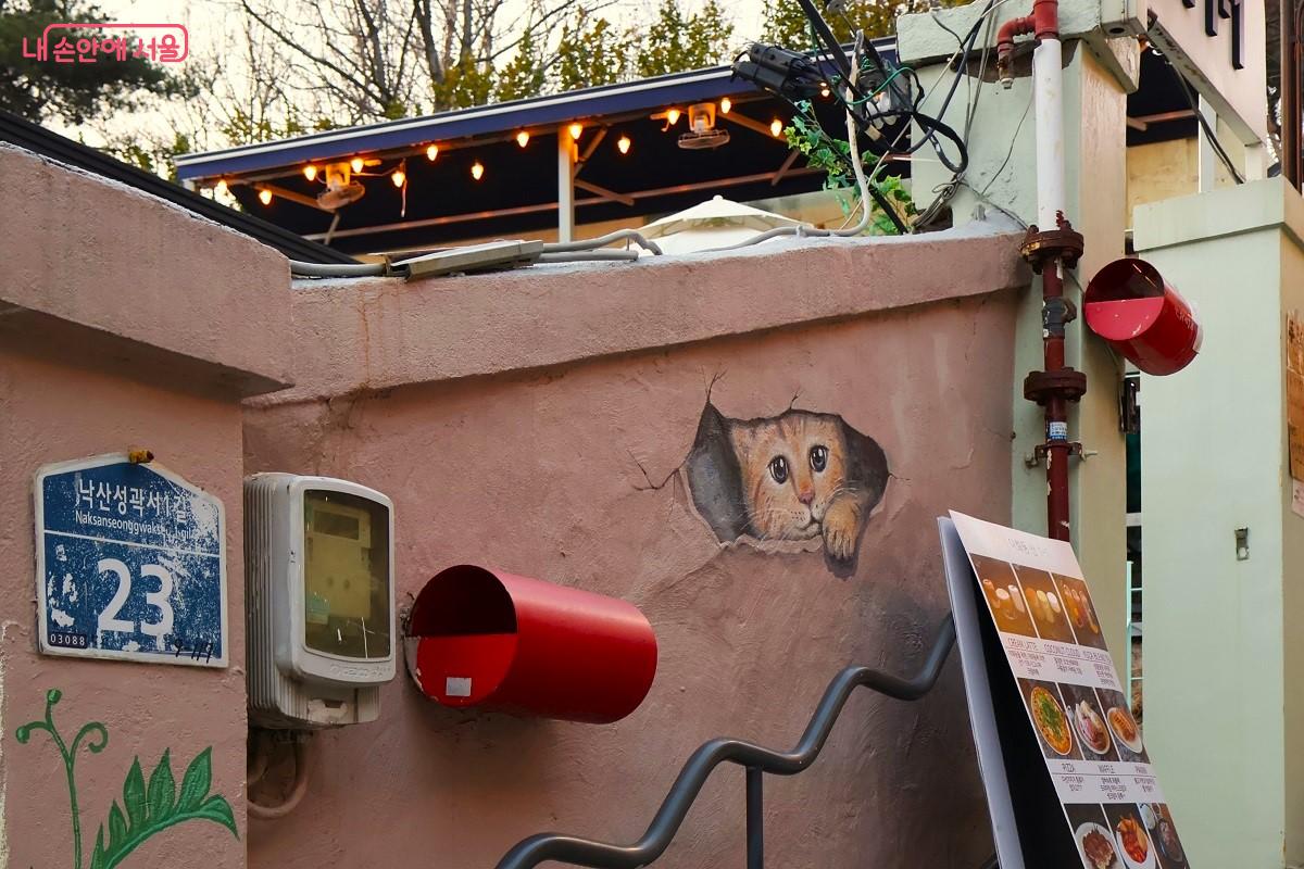 담벼락 구멍 사이로 내다보는 귀여운 고양이 벽화가 작은 미소를 선사한다. &copy;이봉덕