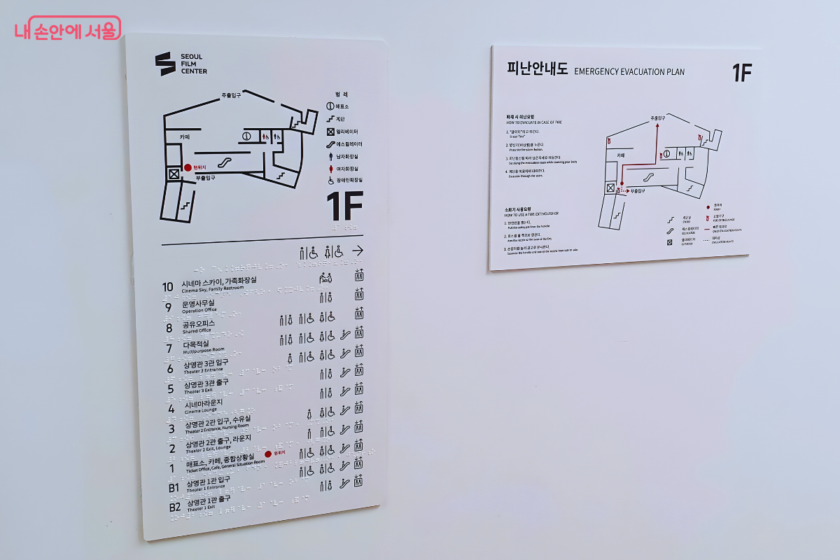 하얀색 벽면에 부착된 서울영화센터의 층별 안내도와 1층 피난 안내도이다. 왼쪽 안내판에는 지하 2층 상영관 1관부터 지상 10층 시네마 스카이까지 각 층의 시설 명칭이 상세히 적혀 있으며 점자 표기가 병행되어 있다. 오른쪽에는 화재 시 대피 경로를 화살표로 표시한 1층 평면도가 부착되어 있다. &copy;신창근