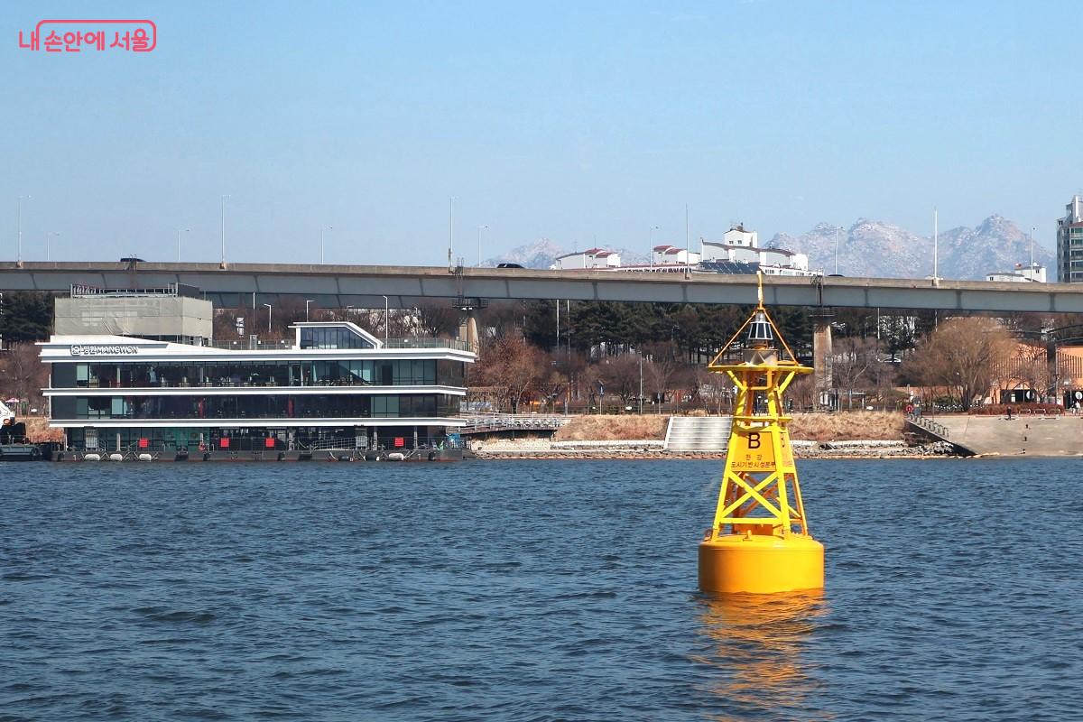 망원선착장을 배경으로, 강물 위에 노란색 항로 표지 부표가 한강의 낭만을 더한다. ⓒ이봉덕