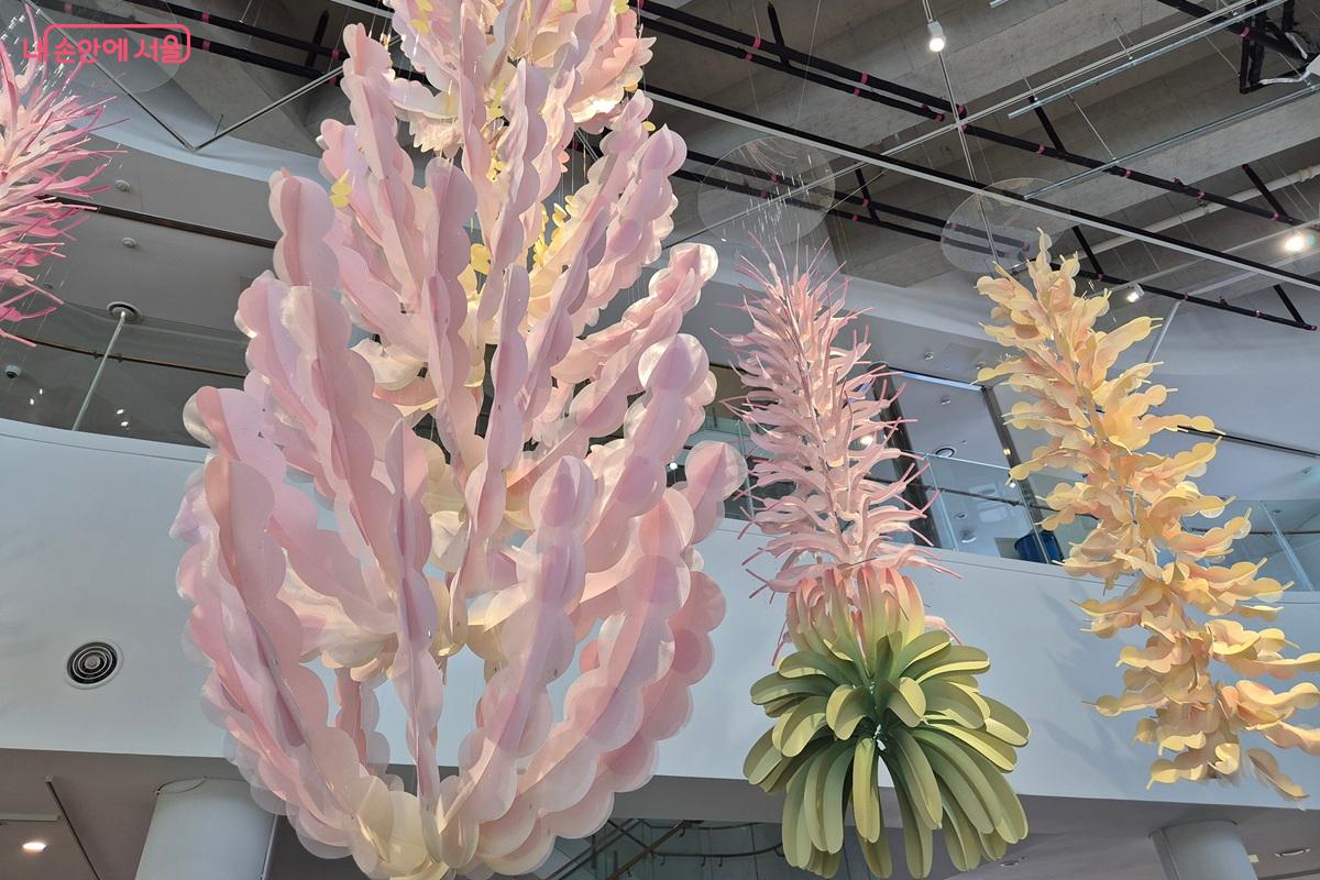 양지윤 작가의 행잉 전시물인 '기원의 모양'이 전시되어 있다. 종이와 한복천을 활용해 꽃을 만들어 공중에서 다양하게 흔들리는 모습이다. ⓒ마가은