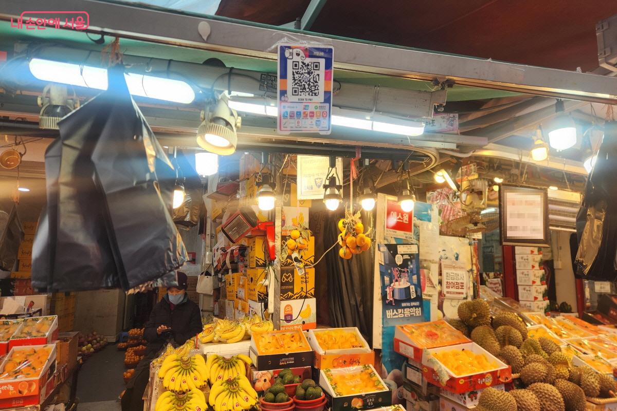 남구로시장 한 과일가게 판매대에 한라봉, 두리안, 바나나 등 다양한 과일이 진열돼 있다. 판매대 상단에는 서울페이 결제를 위한 QR코드 안내판이 함께 부착돼 있다.