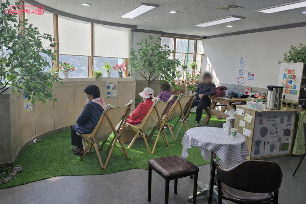 밝은 자연광이 들어오는 실내 공간에서 여러 명의 이용자들이 창가를 향해 나란히 앉아 족욕기를 이용하며 편안히 휴식을 취하고 있다. 의자들은 잔디처럼 꾸며진 바닥 위에 놓여 있고, 창가에는 작은 화분들이 줄지어 있어 따뜻하고 편안한 분위기를 만든다. &copy;최동열