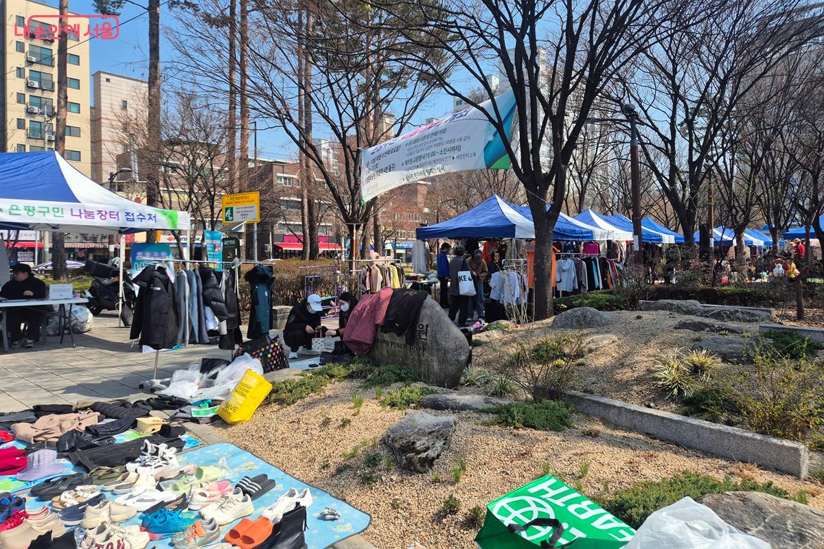 공원 내의 산책로를 따라 나눔장터가 길게 형성되어 있다. 주민들이 길을 오가며 제품을 구경하고 있다. ©마가은