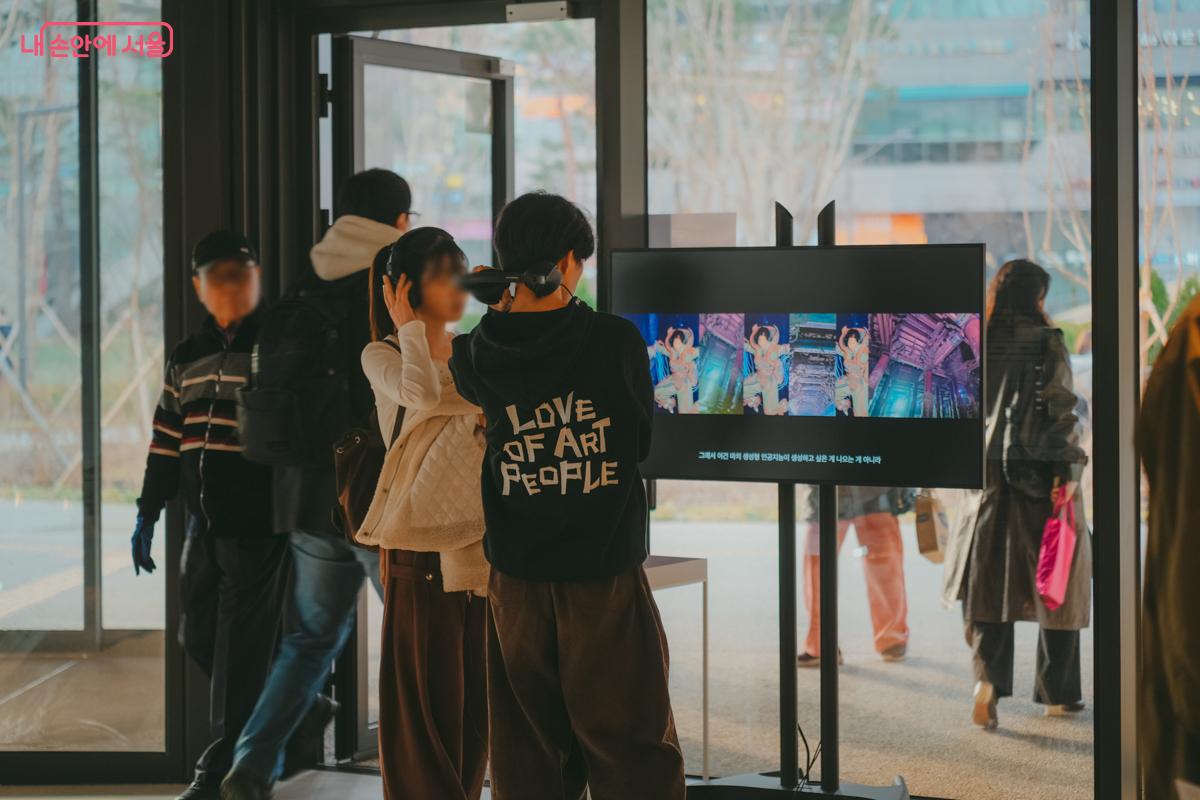 미술관 로비에서 헤드폰을 쓴 청년이 스크린에서 재생되는 화려한 색감의 미디어아트 영상을 집중해서 감상하고 있다.