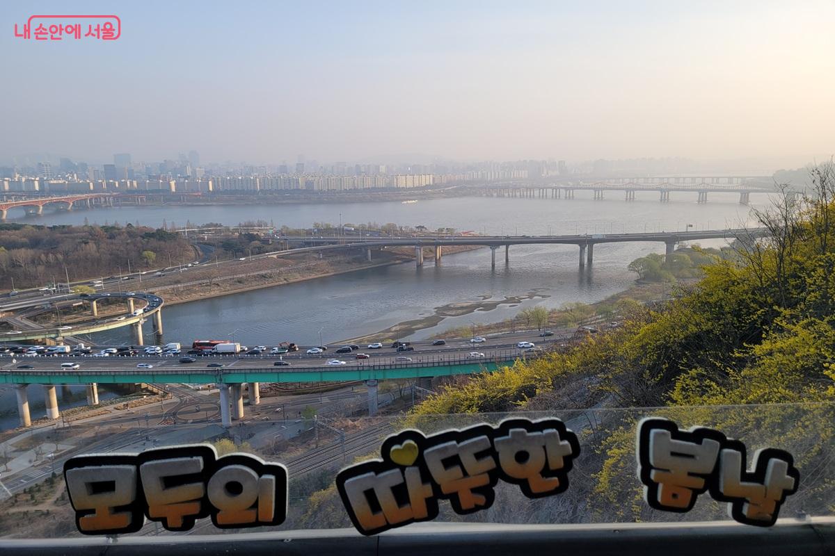 &lsquo;모두의 따뜻한 봄날&rsquo;이라는 문구 너머로 바라본 한강 풍경 ⓒ조연