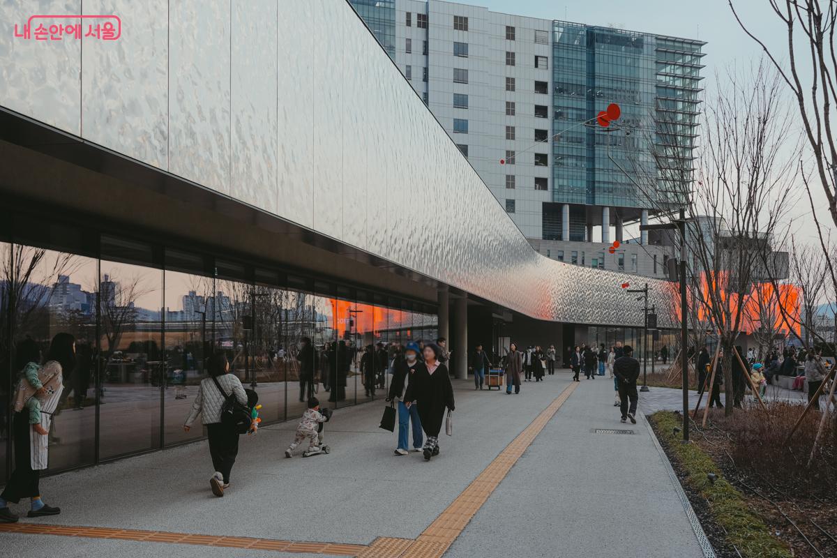 서서울미술관 외부 전경. 은빛으로 빛나는 물결무늬의 곡선형 외벽을 따라 시민들이 산책하고 있다.