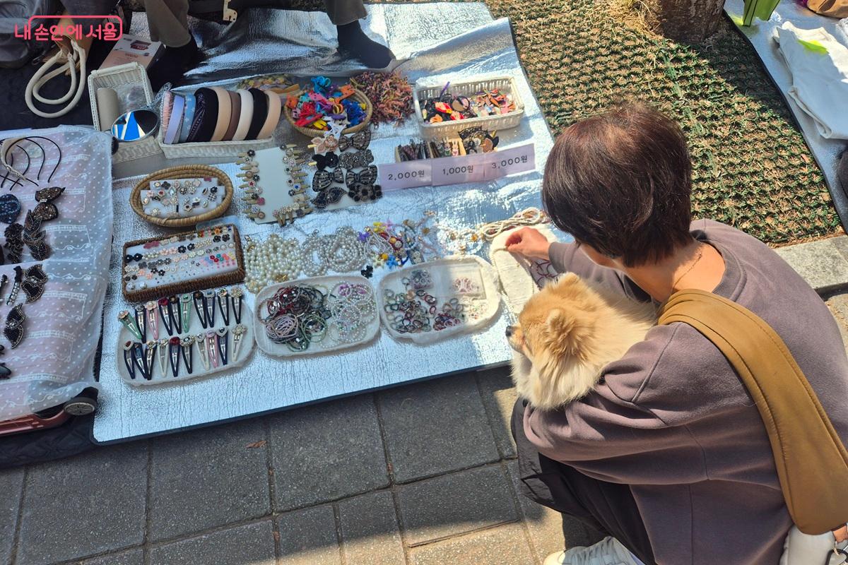 반려견과 산책하던 시민이 공원 장터에 들러 물품을 살펴보고 있다. 반려견도 품에 안겨 함께 바라보고 있다. ©마가은