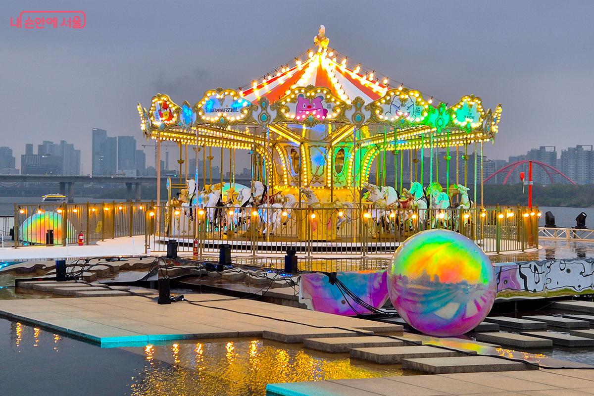 한강 위 거대한 회전목마에서 직접 체험하는 놀이와 레이저와 불꽃 등으로 펼쳐지는 마법의 판타지쇼를 경험하는 &lsquo;시그니처쇼(SIGNATURE SHOW)&rsquo;