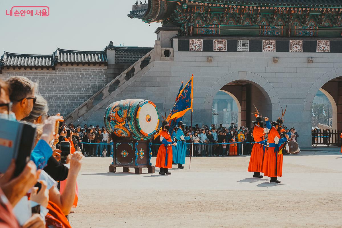 화려한 용 무늬가 그려진 대형 북을 치고 있는 붉은 의상의 수문군과 이를 지켜보는 관람객들 사진