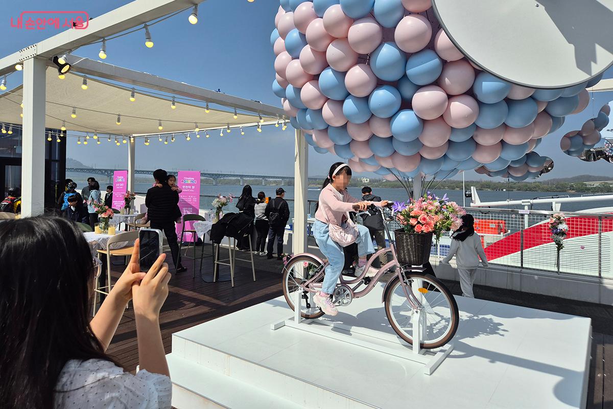 구름 풍선 밑에 자리한 노을 자전거를 타며 사진을 찍는 어린이들 ©이혜숙