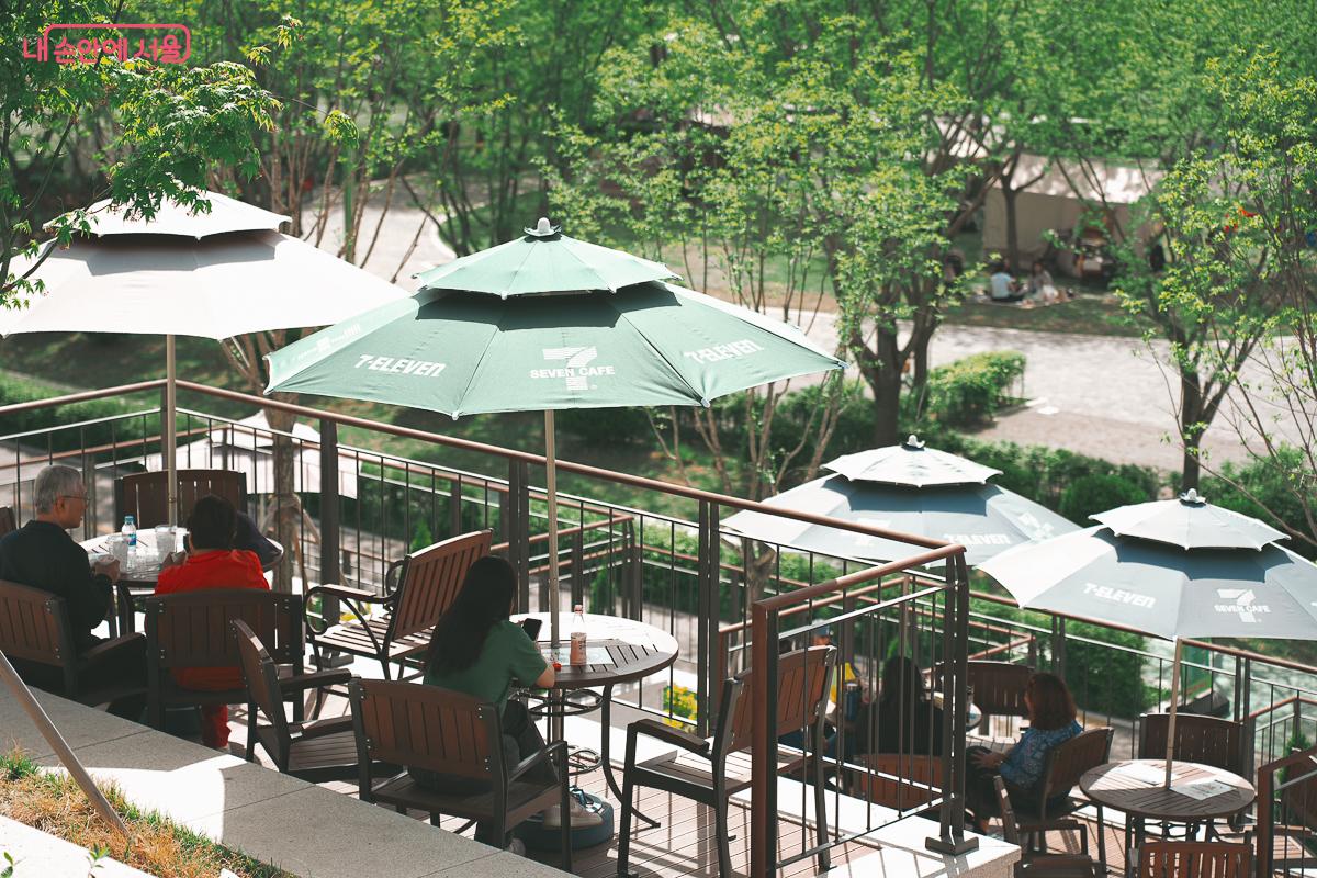 하얀색과 초록색 대형 파라솔 아래 원형 테이블과 의자가 놓여 있는 야외 테라스에서 시민들이 다과를 즐기고 있다. &copy;김성무