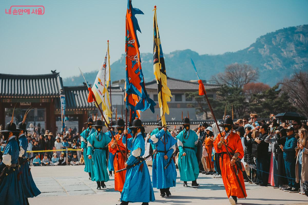푸른색과 붉은색 옷을 입은 수문군들이 긴 창과 깃발을 들고 행렬을 맞추어 걸어가는 사진