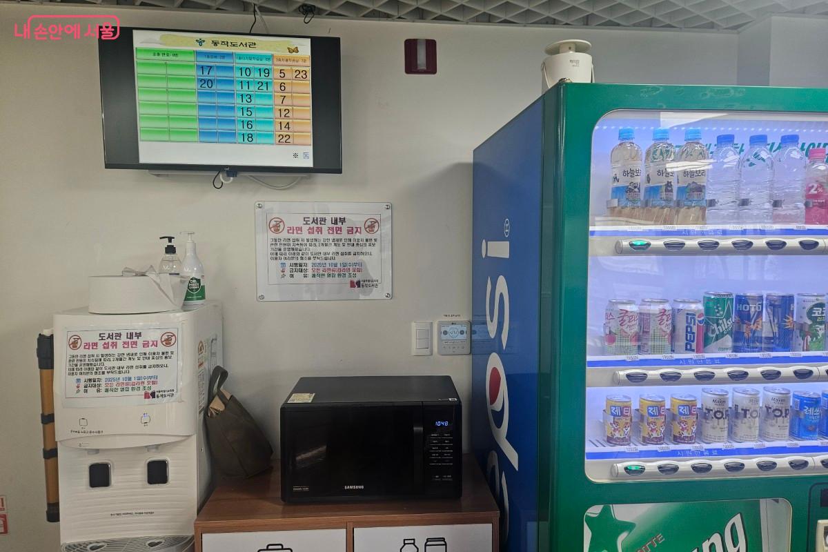 카페테리아의 안내문이다. 좌측 위의 전광판은 좌석 대기를 하고 있는 이용대기 고객의 번호판을 보여주며, 좌측 아래에는 정수기와 전자레인지가 있으며, 우측 중간에는 자판기가 있다.