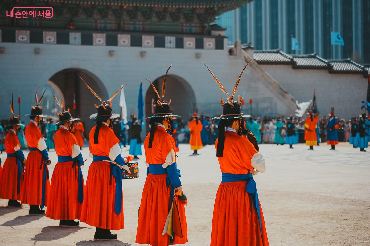 화려한 깃털이 꽂힌 모자를 쓰고 붉은 옷을 입은 대원들의 늠름한 뒷모습과 교대의식 현장 전경
