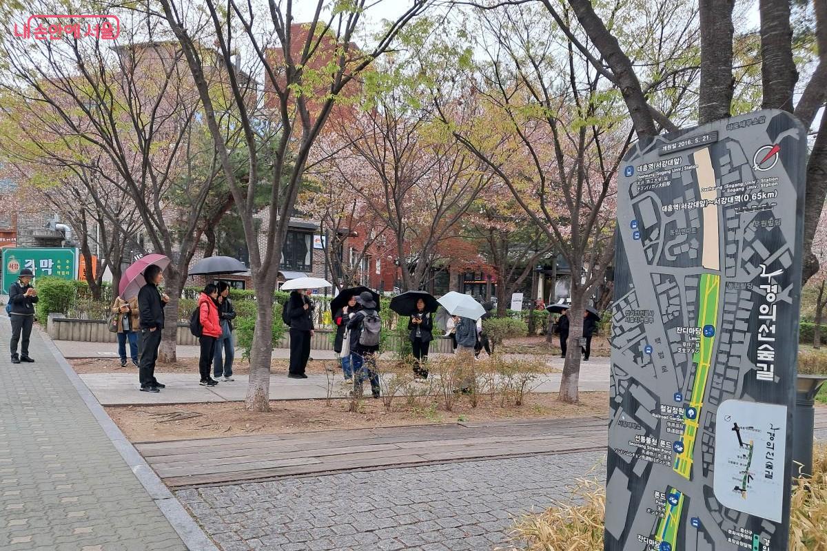 우산을 쓴 채 경의선 숲길에 마주 서서 안내 요원의 설명에 집중하는 방문객