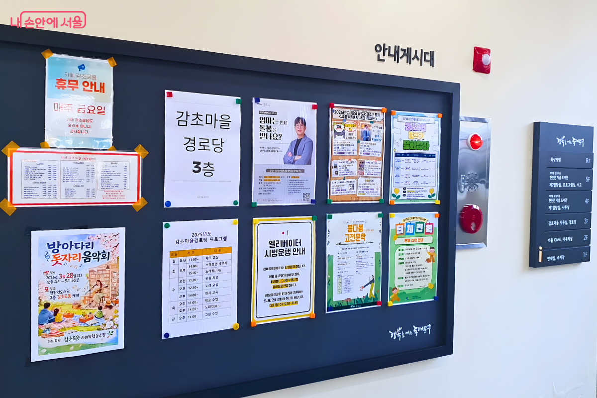 도서관 건물 1층 내부 벽면에 설치된 안내 게시판과 층별 안내판의 모습이다. 게시판에는 카페 휴무 안내, 경로당 프로그램 일정표, 도서관 주간 행사 등 마을 소식을 알리는 다양한 포스터들이 부착되어 있다. 우측에는 1층 안내실부터 옥상(RF)까지 각 층의 시설 명칭이 적힌 검은색 안내판이 나란히 배치되어 방문객들의 이용을 돕는다.