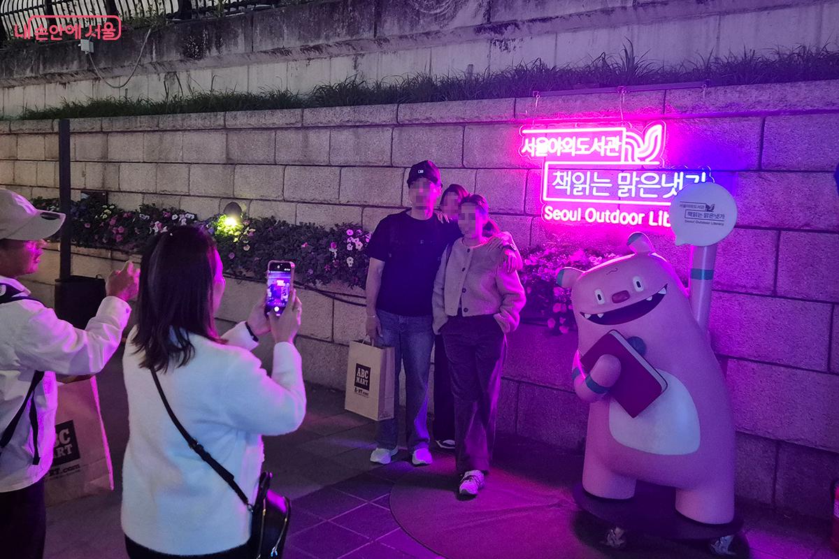 &lsquo;책읽는 맑은냇가&rsquo; LED 와 해치 인형을 배경으로 기념사진을 찍는 시민들의 모습