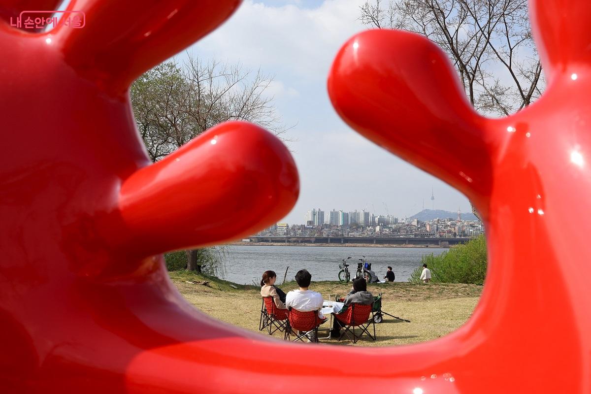 강렬한 붉은 색 조각품 사이로 한강의 봄을 만끽하는 시민들과 멀리 남산타워가 한 폭의 그림처럼 담겼다. &copy;이봉덕