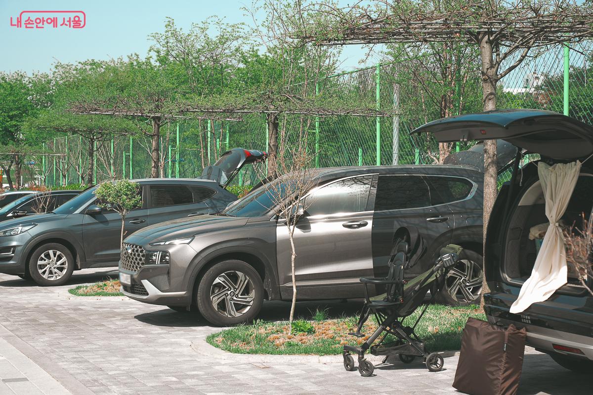 전용 주차 구역에 주차된 SUV 차량들의 트렁크가 열려 있고 유모차와 캠핑 용품들이 곁에 놓여 있다. &copy;김성무