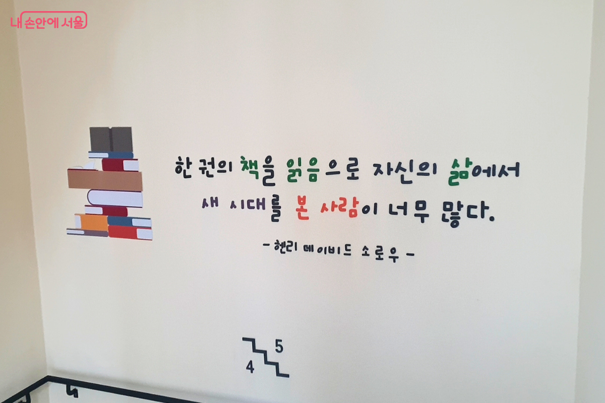도서관 4층과 5층 사이 계단 복도 벽면에 적힌 명언 문구이다. 쌓여 있는 책 그림 옆으로 "한 권의 책을 읽음으로 자신의 삶에서 새 시대를 본 사람이 너무 많다"는 헨리 데이비드 소로우의 글귀가 적혀 있다. 벽면 하단에는 현재 위치가 4층과 5층 사이임을 알리는 층수 표시와 계단 아이콘이 그려져 있다.
