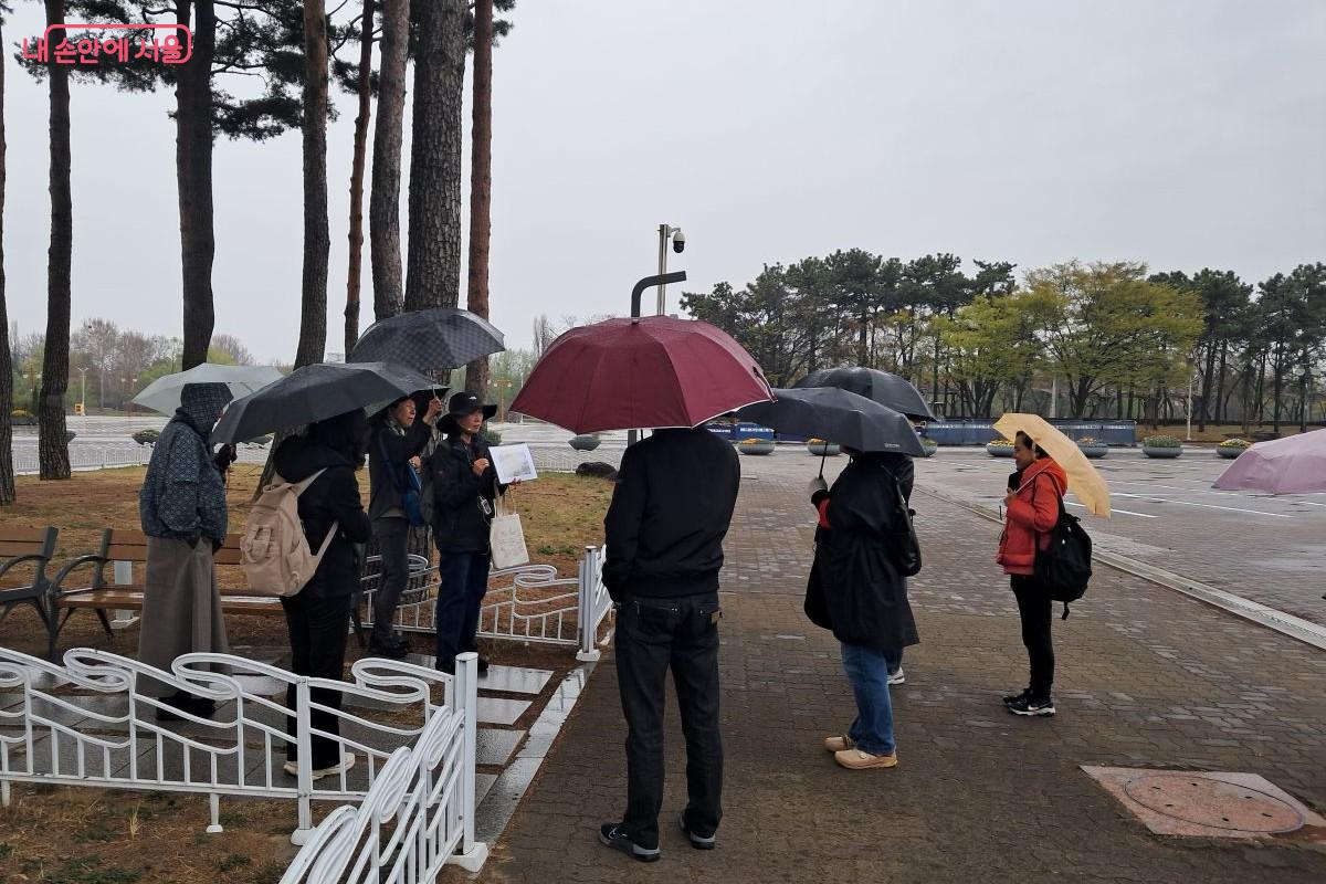 월드컵 공원에서 방문객이 옹기종기 우산을 쓰고 가이드의 설명을 듣고 있는 모습