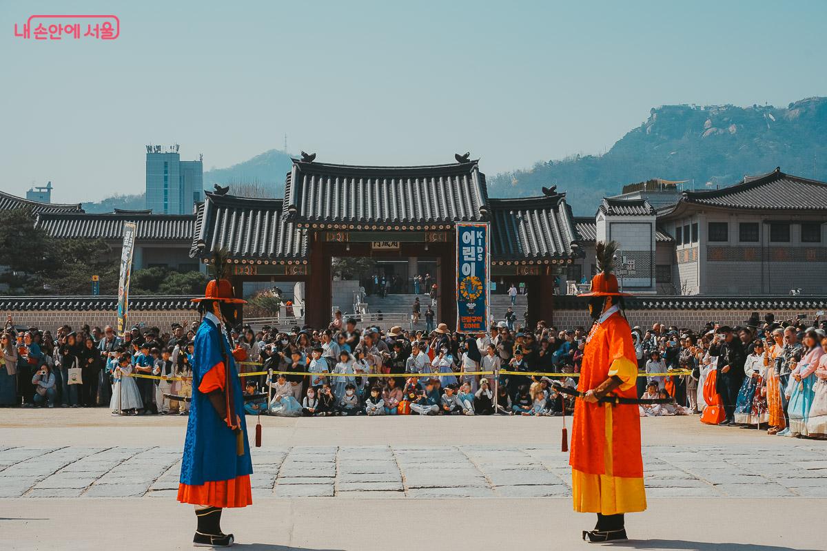 넓은 광장 가운데 서로를 마주 보며 칼을 차고 서 있는 두 수문장과 그 뒤를 가득 채운 관람객들